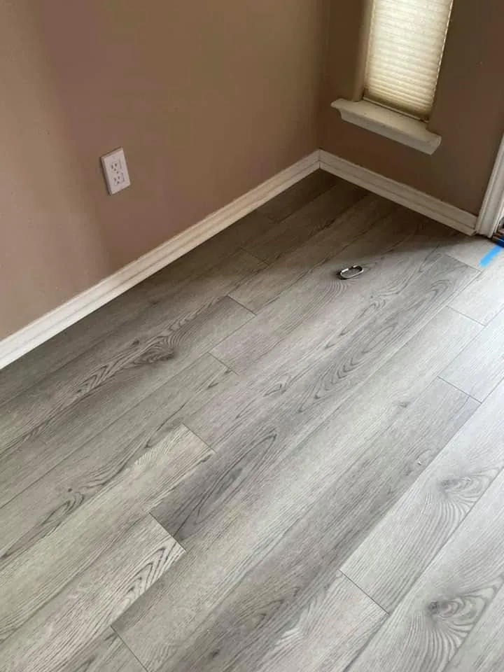 Gray wood look laminate floor laid in a bedroom corner with fresh baseboard