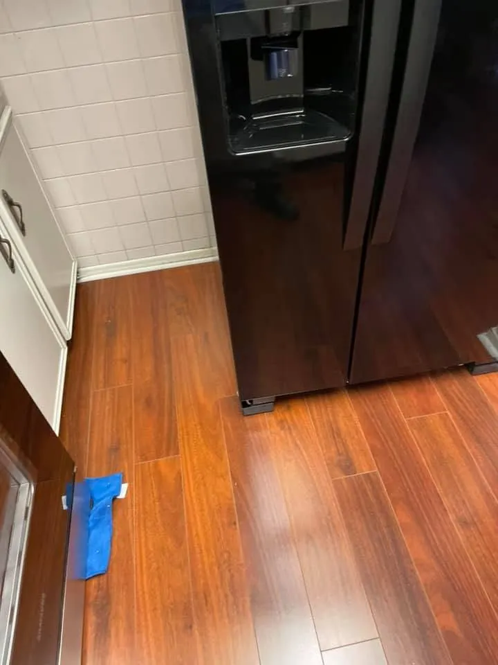 Glossy laminate flooring laid in a kitchen beside the refrigerator