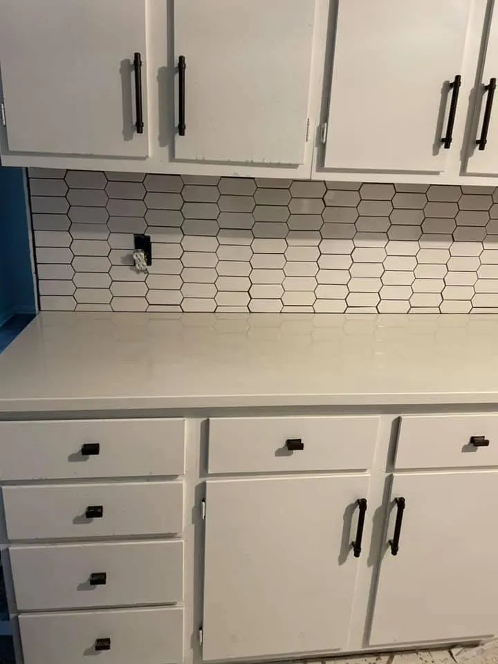 White kitchen cabinets with a light countertop and a hexagon tile backsplash