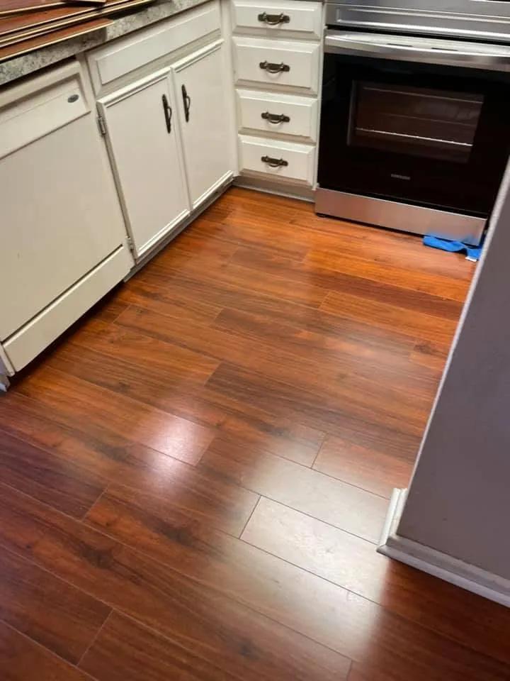 Warm toned laminate floor in a kitchen with white cabinets and a range
