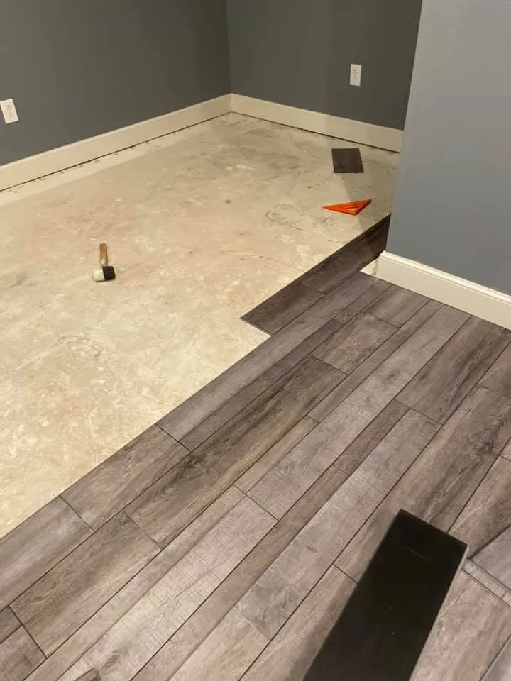 Gray planks being laid across a tiled subfloor with a clean edge